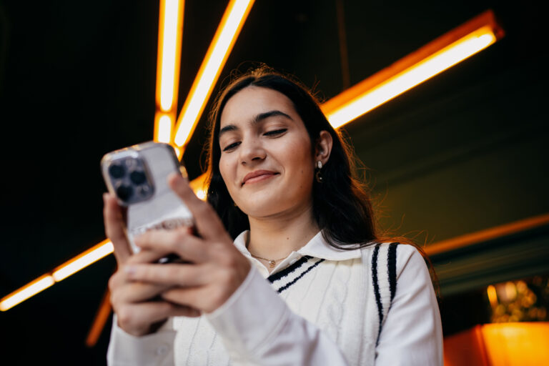 Woman smiling while reading something on smartphone screen, emphasizing satisfaction and ease of digital interaction in modern tech culture.